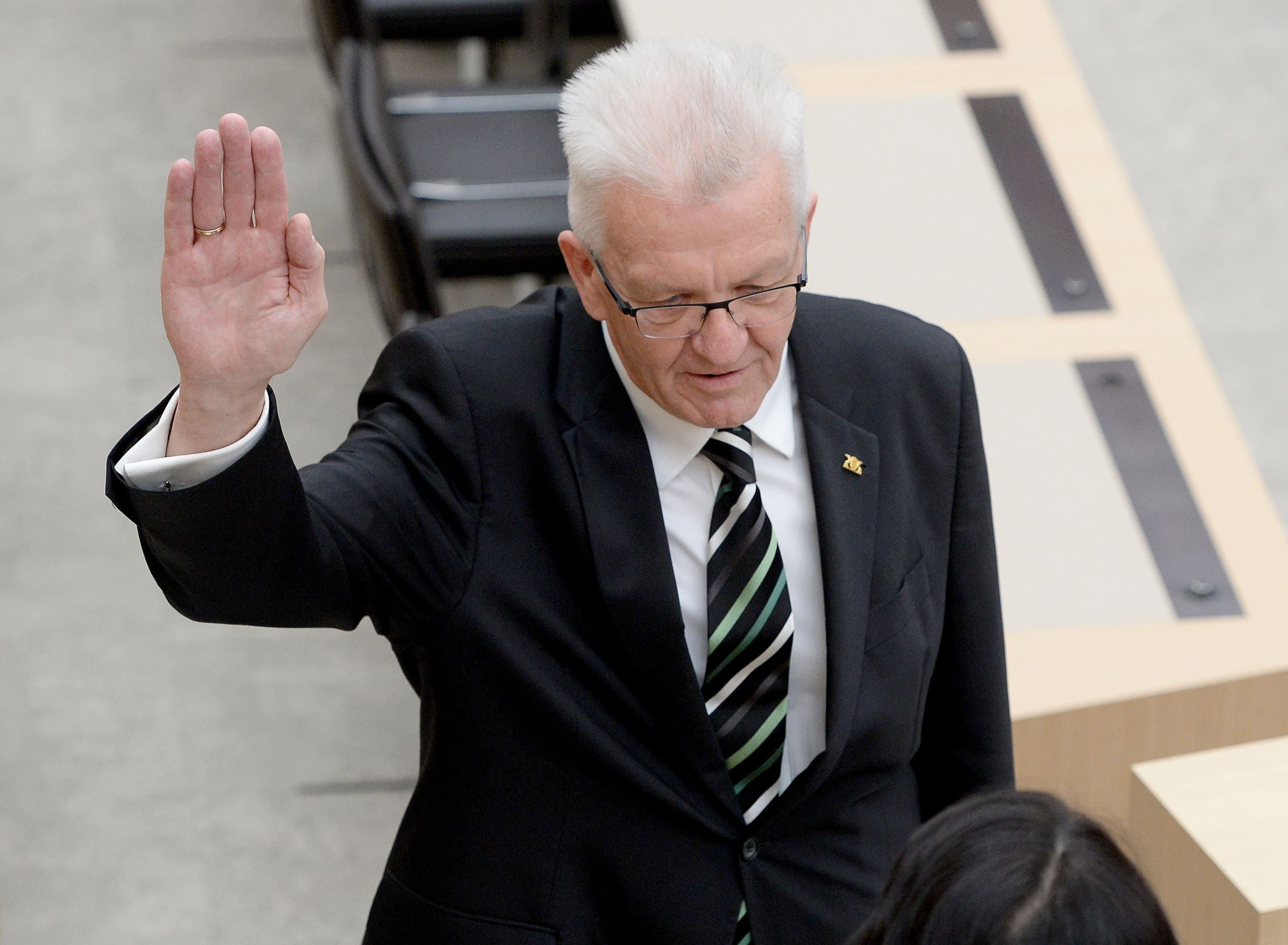 Winfried Kretschmann hält im Plenarasaal seine rechte Hand zur Vereidigung hoch.